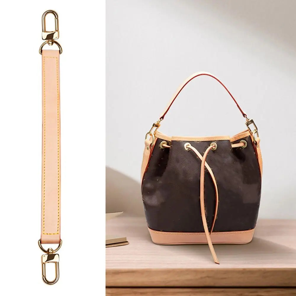 A black leather handbag with a light pink lining and a tan leather strap is displayed on a wooden surface.