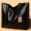 A black metallic crocodile print zipper tote bag displayed on a light background.