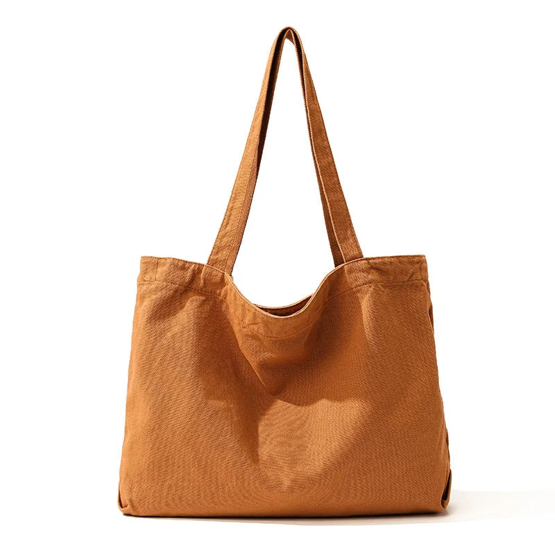 A brown canvas shoulder tote bag with long handles is shown against a white background.