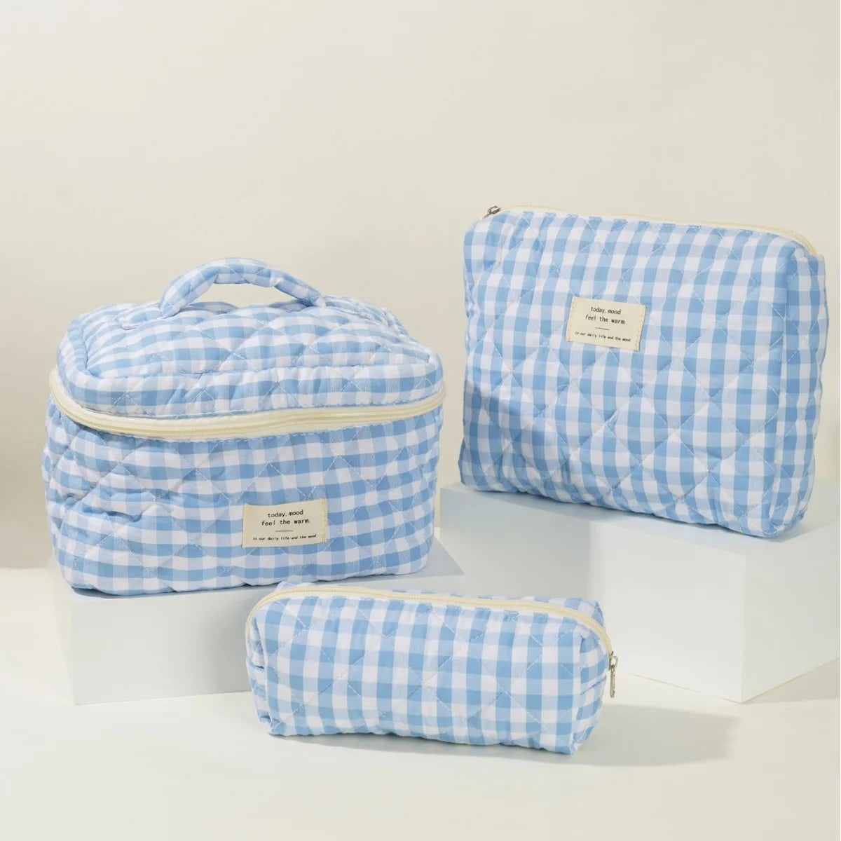 A set of light blue and white checkered quilted cotton makeup organizers in various sizes.
