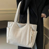 A light beige ribbed casual corduroy handbag carried by a person wearing a black coat.