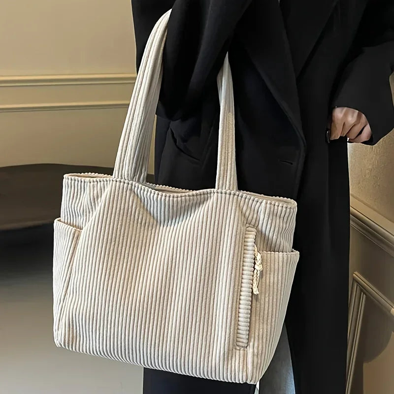 A light beige ribbed casual corduroy handbag carried by a person wearing a black coat.