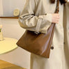 A woman holds a brown PU leather slouchy hobo shoulder bag while wearing a beige trench coat.