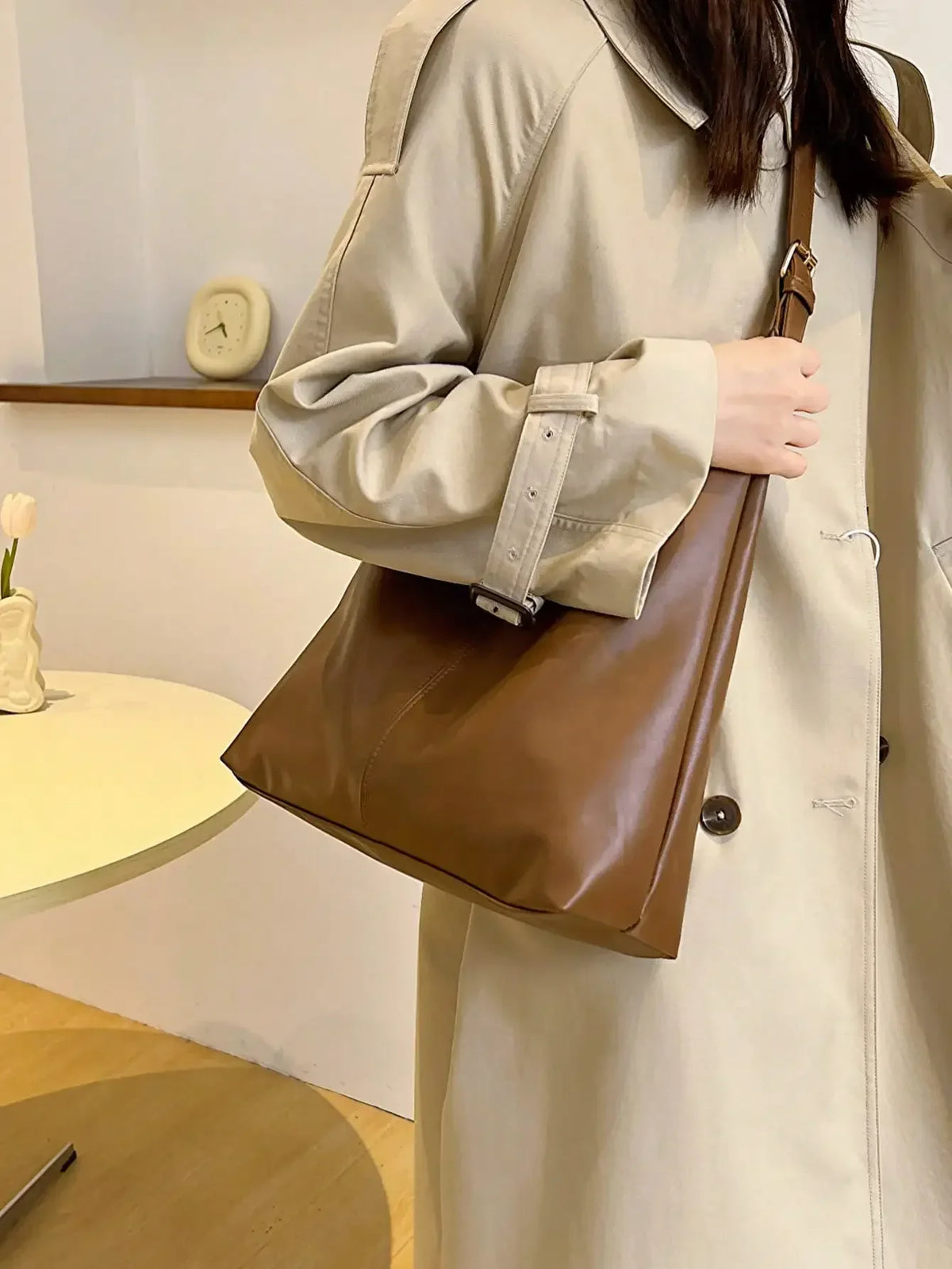 A woman holds a brown PU leather slouchy hobo shoulder bag while wearing a beige trench coat.