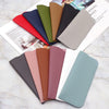 Colección de fundas para gafas de cuero PU en varios tonos de verde, rosa, marrón y gris sobre una superficie blanca.