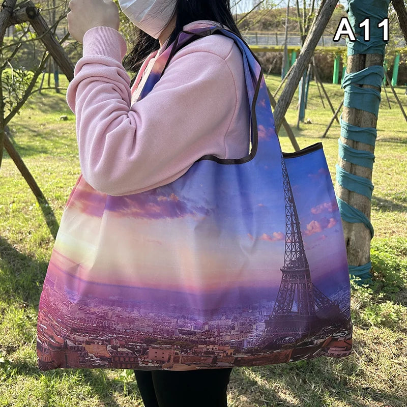 A person holds a large tote bag featuring a sunset cityscape of Paris, France.