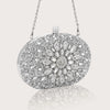 Pochette clutch en strass argenté avec une bandoulière, présentée sur un fond gris clair.