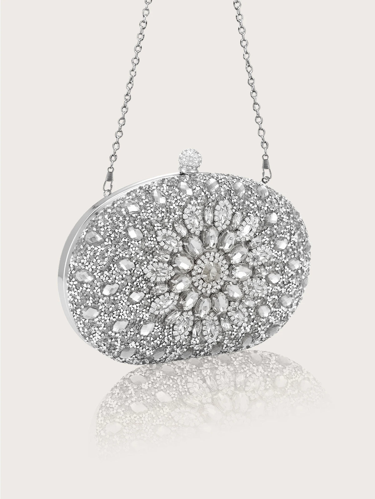 Pochette clutch en strass argenté avec une bandoulière, présentée sur un fond gris clair.