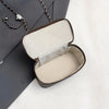 A light beige woven crossbody bag with a dark brown leather strap is shown open against a white background.