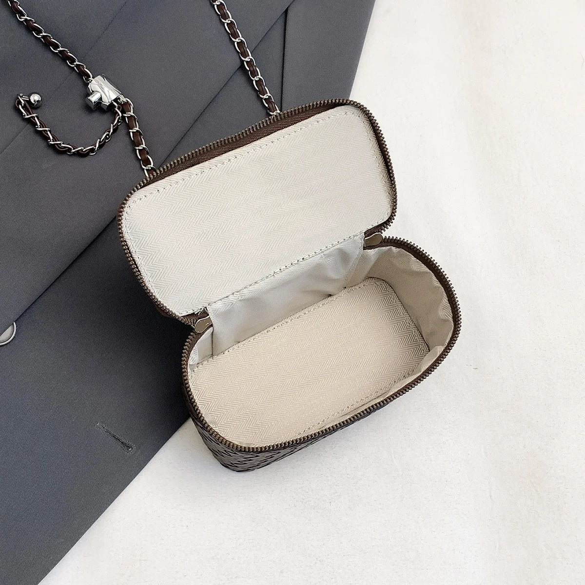 A light beige woven crossbody bag with a dark brown leather strap is shown open against a white background.