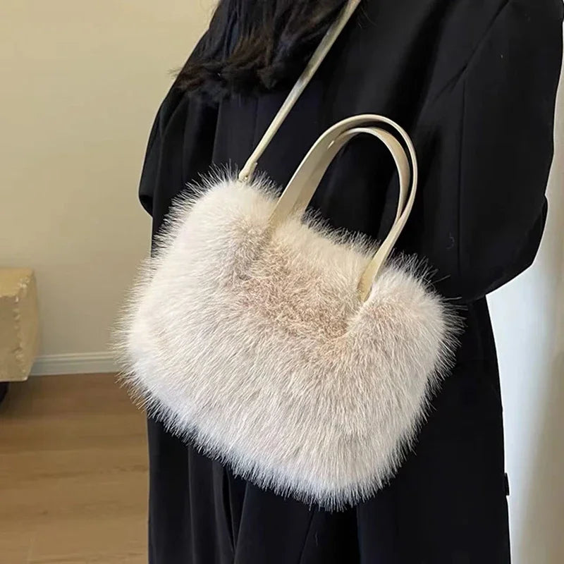 A white plush faux fur tote bag with a light leather crossbody strap is held by a person wearing a black garment.