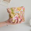 A hand holds a floral canvas makeup bag with pink and green botanical print against a white background.