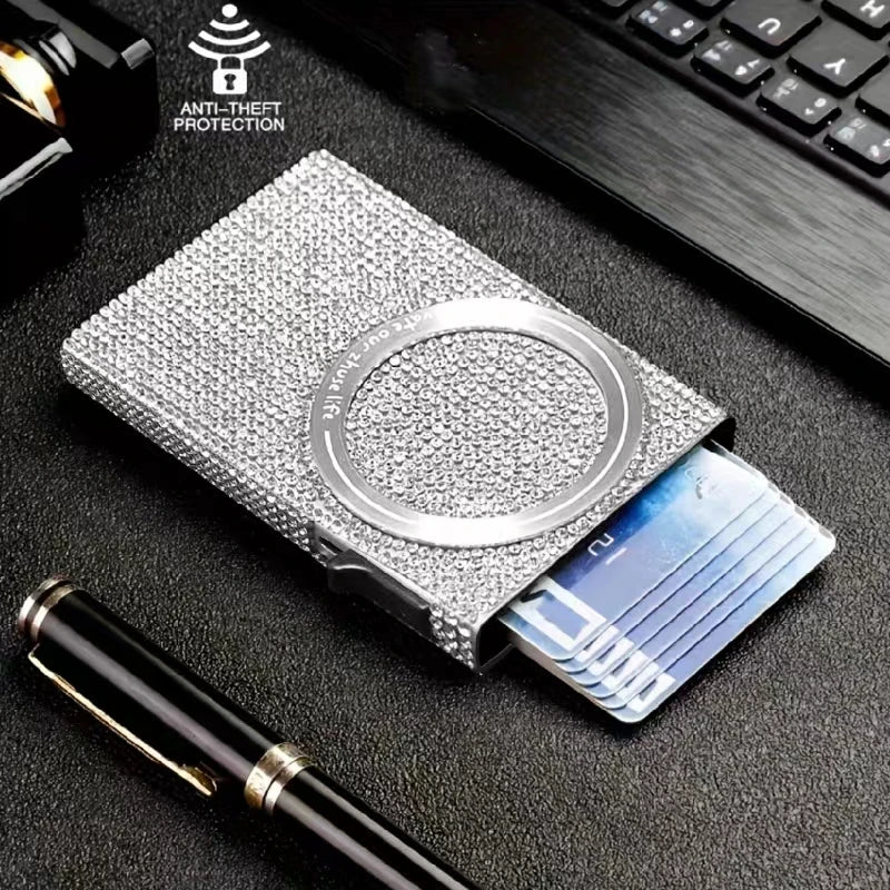 A silver magnetic card holder wallet with a slot for credit cards and a pen on a dark surface.