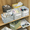 A collection of storage baskets and fabric items on a wooden shelf, including a black woven basket, a yellow basket, and seve