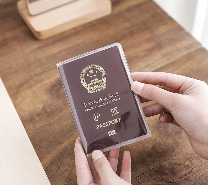 A hand holds a dark purple passport card sleeve with gold embossing on a wooden table.