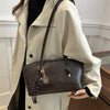 A woman holds a brown leather tote bag against a light beige trench coat.