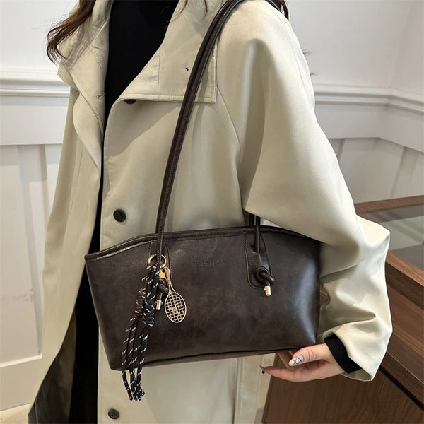 A woman holds a brown leather tote bag against a light beige trench coat.