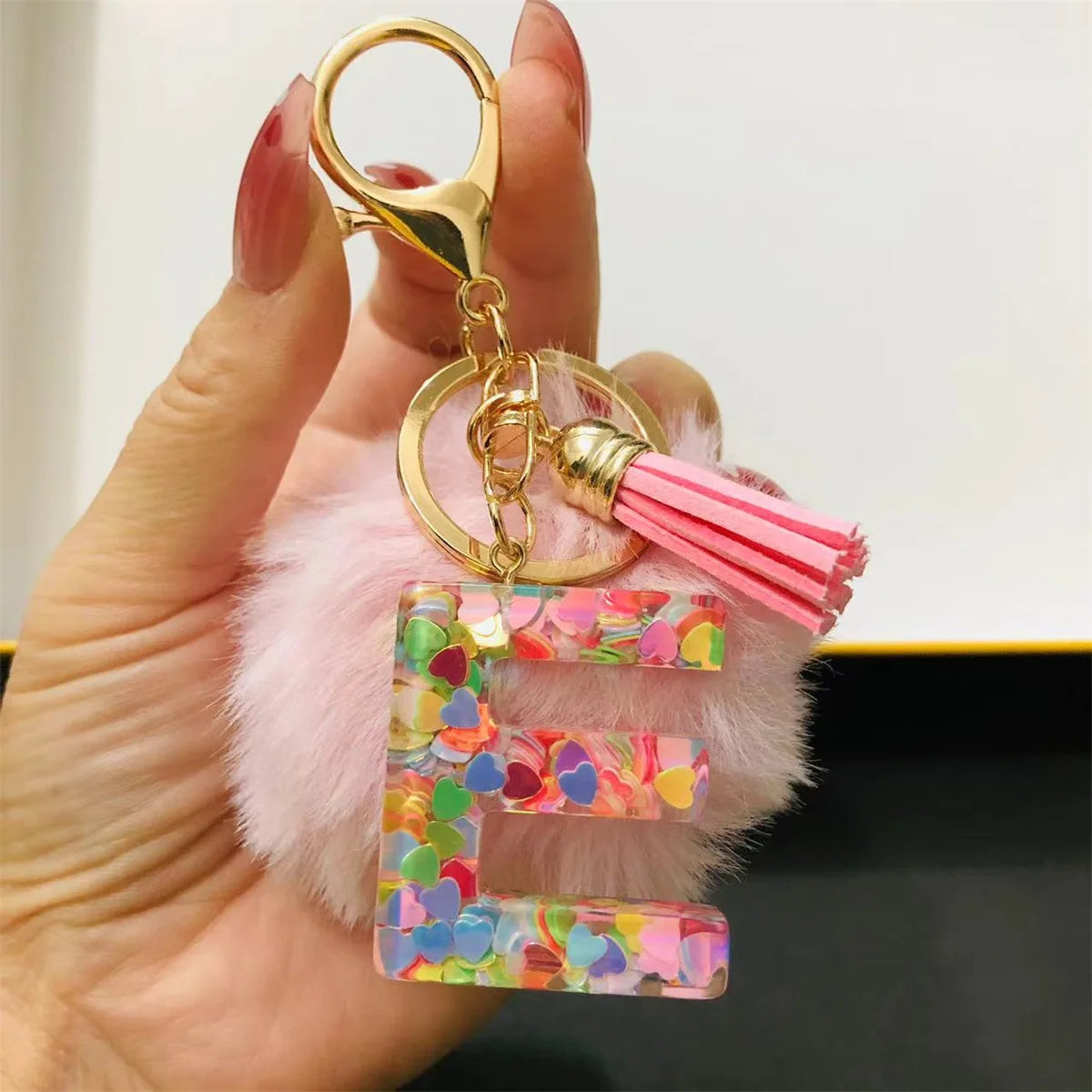 A hand holds a custom initial letter keychain featuring a shiny resin pendant and pink alphabet charm.