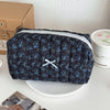 A dark blue floral patterned quilted cosmetic bag resting on a white surface next to a white container.