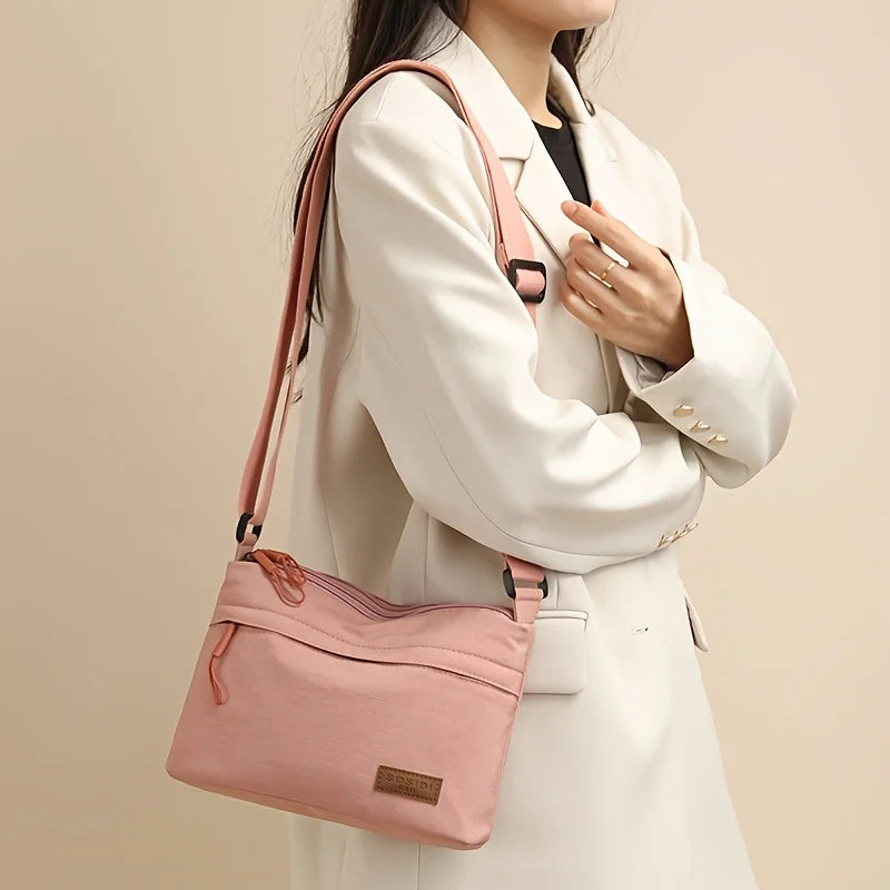 A woman holds a pink nylon crossbody shoulder bag against a light beige coat.