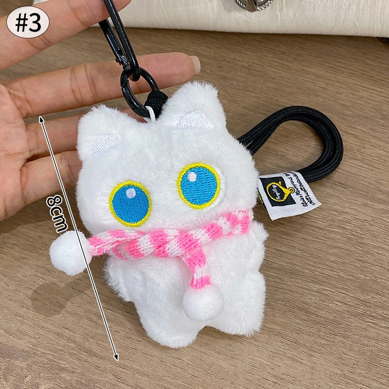 Colgante llavero de peluche de gato blanco esponjoso con ojos azules y una cinta rosa contra un fondo de madera.