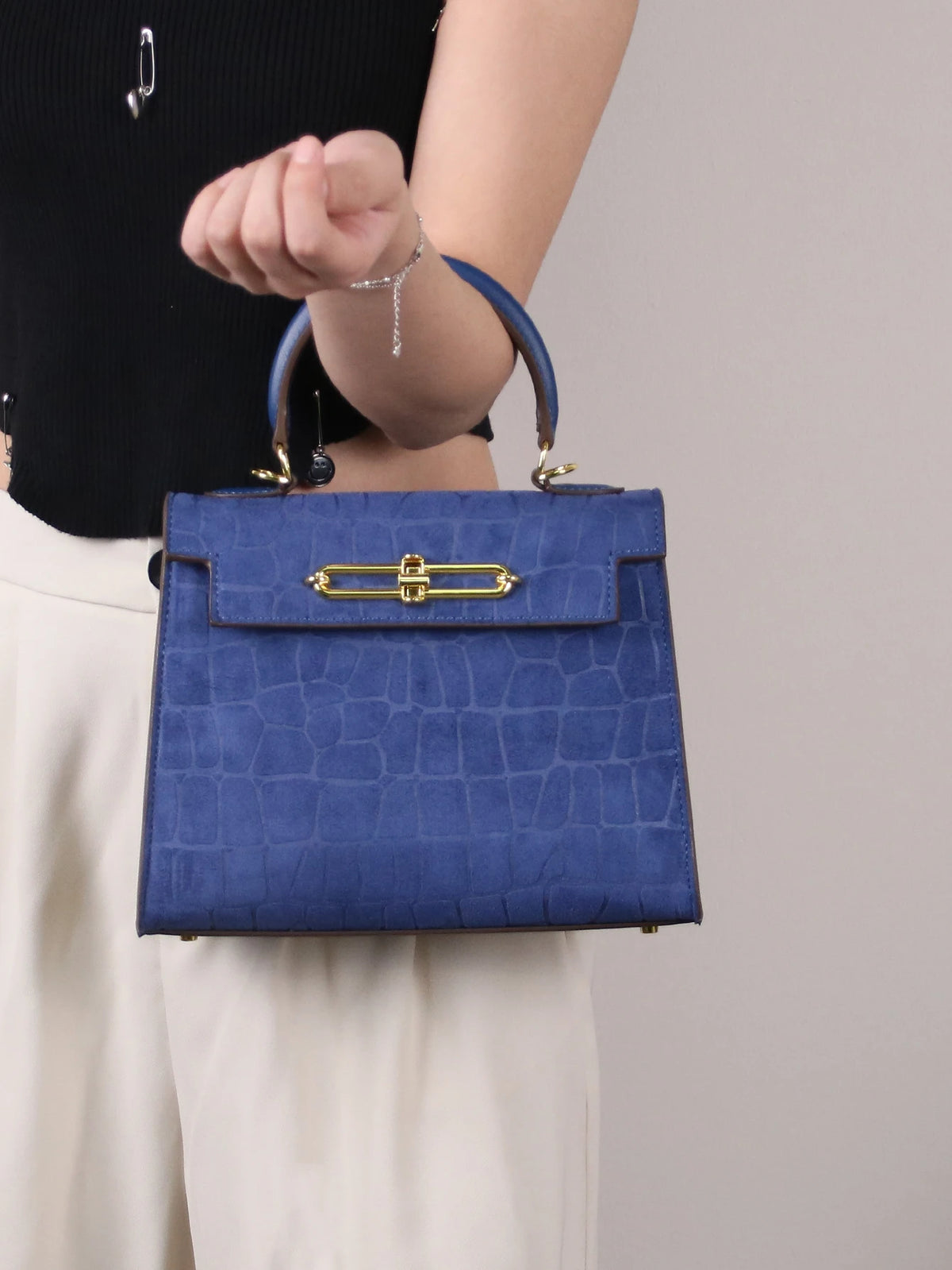 A navy blue crocodile pattern tote bag with gold hardware carried by a woman.