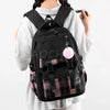 Black canvas backpack with a plaid pattern and a pink pom-pom charm worn by a person.