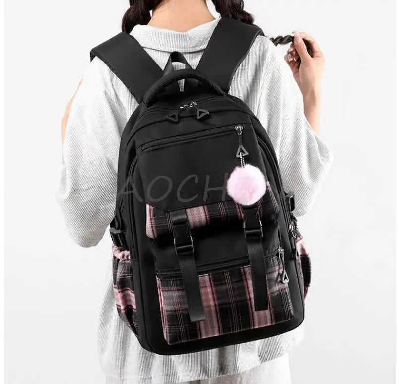 Black canvas backpack with a plaid pattern and a pink pom-pom charm worn by a person.