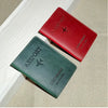 A red leather passport holder and a dark green leather passport wallet are displayed on a light surface.