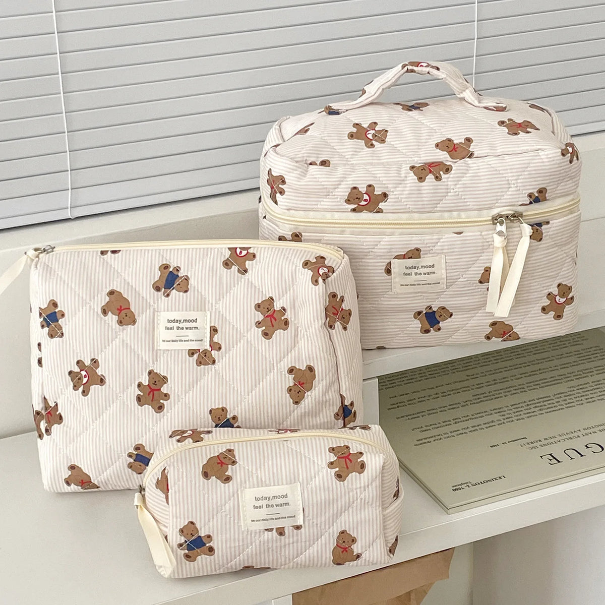 A beige striped cosmetic makeup bag with a light pink lining and bear embroidery is displayed on a white surface.