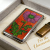 An Art Deco metal card case with a vibrant floral design rests in a light gray box.
