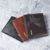 A brown leather wallet with an embossed eagle design is shown lying on a light gray surface.