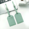 Two mint green PU leather luggage tags with silver hardware resting on a white desk next to a laptop.