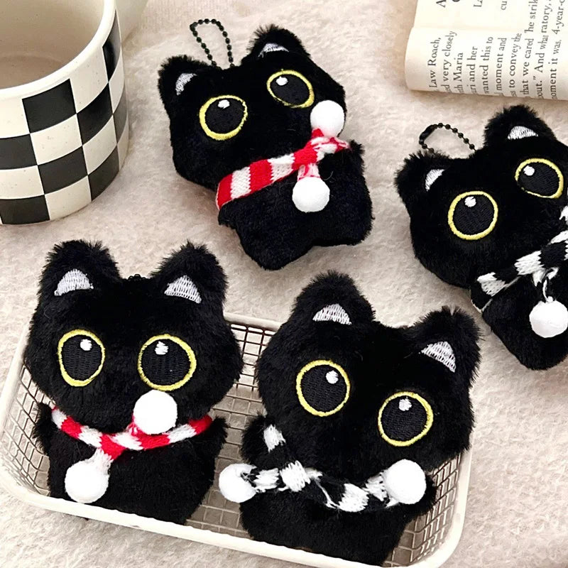Colección de colgantes y llaveros de peluche de gato negro con detalles en blanco y rojo, exhibidos en una bandeja blanca.