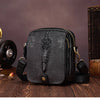 Black genuine cow leather crossbody bag for men resting on a wooden surface.