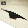 A close-up view of a cream colored Oxford cloth tote bag with a black interior and a leather accent.