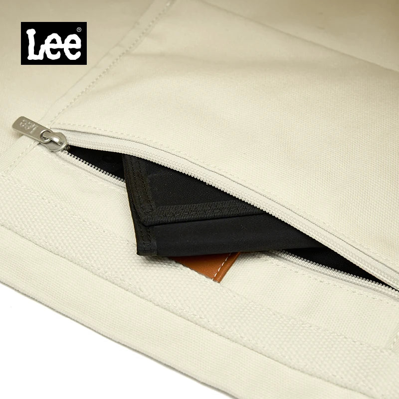 A close-up view of a cream colored Oxford cloth tote bag with a black interior and a leather accent.