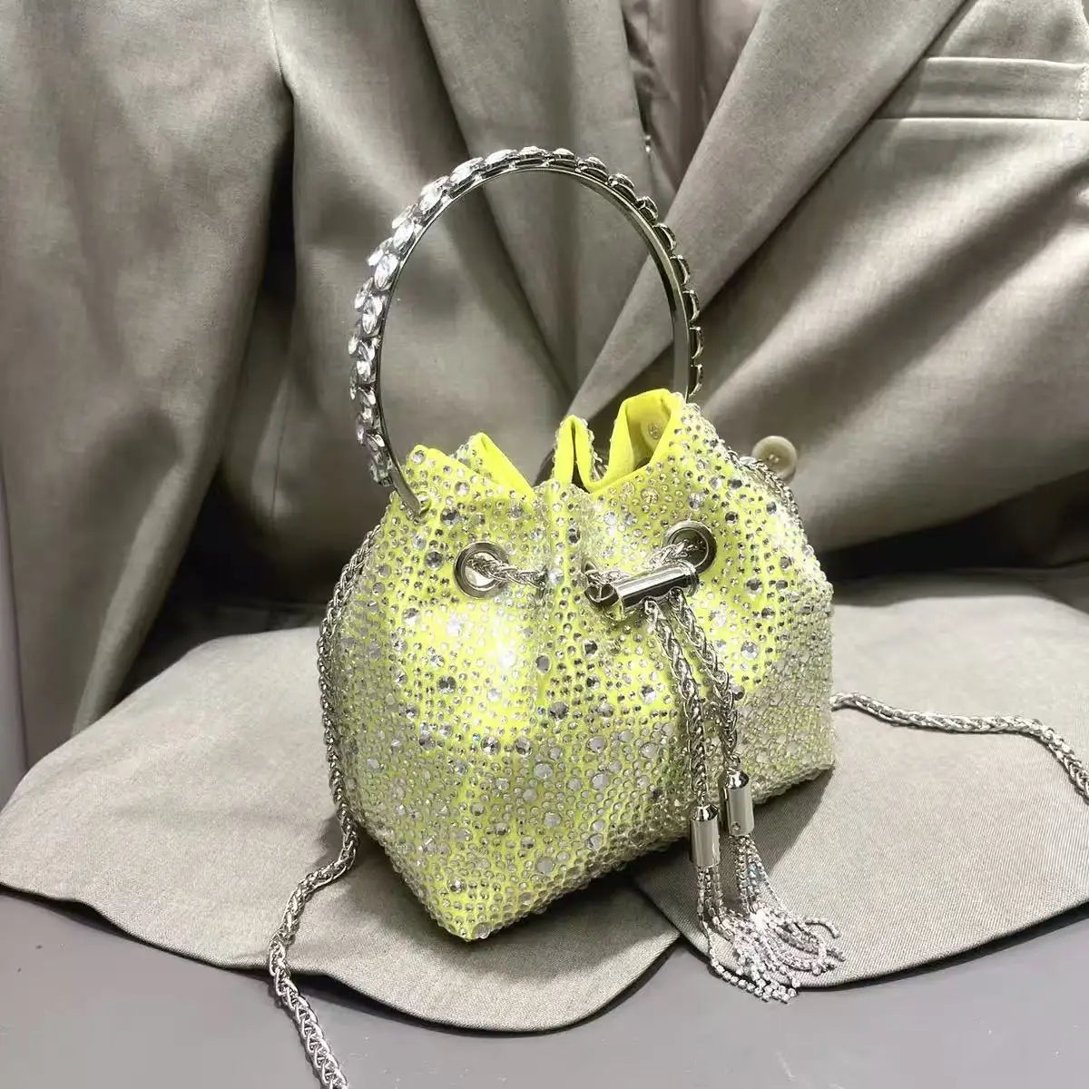 A yellow crystal-embellished evening clutch with a silver chain strap is displayed on a light gray fabric.