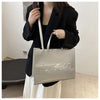A woman holds a silver tote bag in front of her while wearing a black blazer and a white skirt.