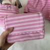 A hand holds a pink striped makeup bag with a flip-top mirror, next to pink striped clothing.