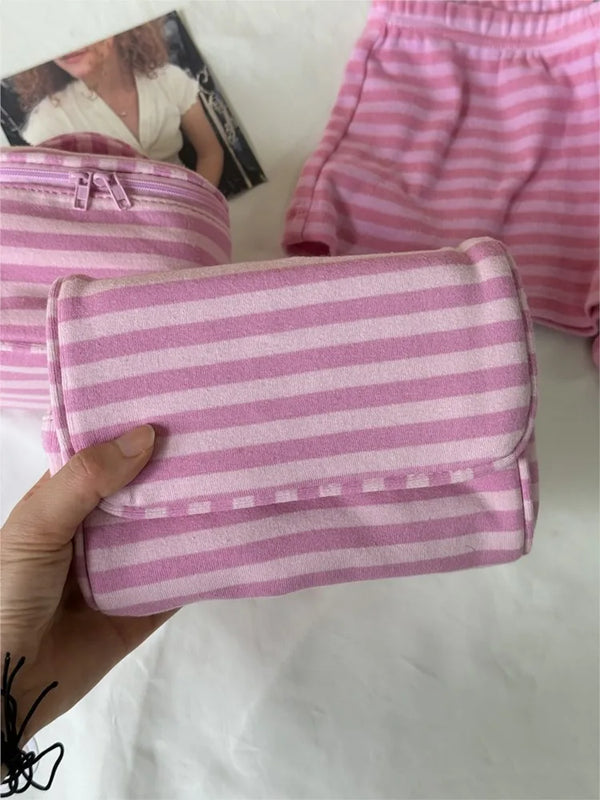 A hand holds a pink striped makeup bag with a flip-top mirror, next to pink striped clothing.