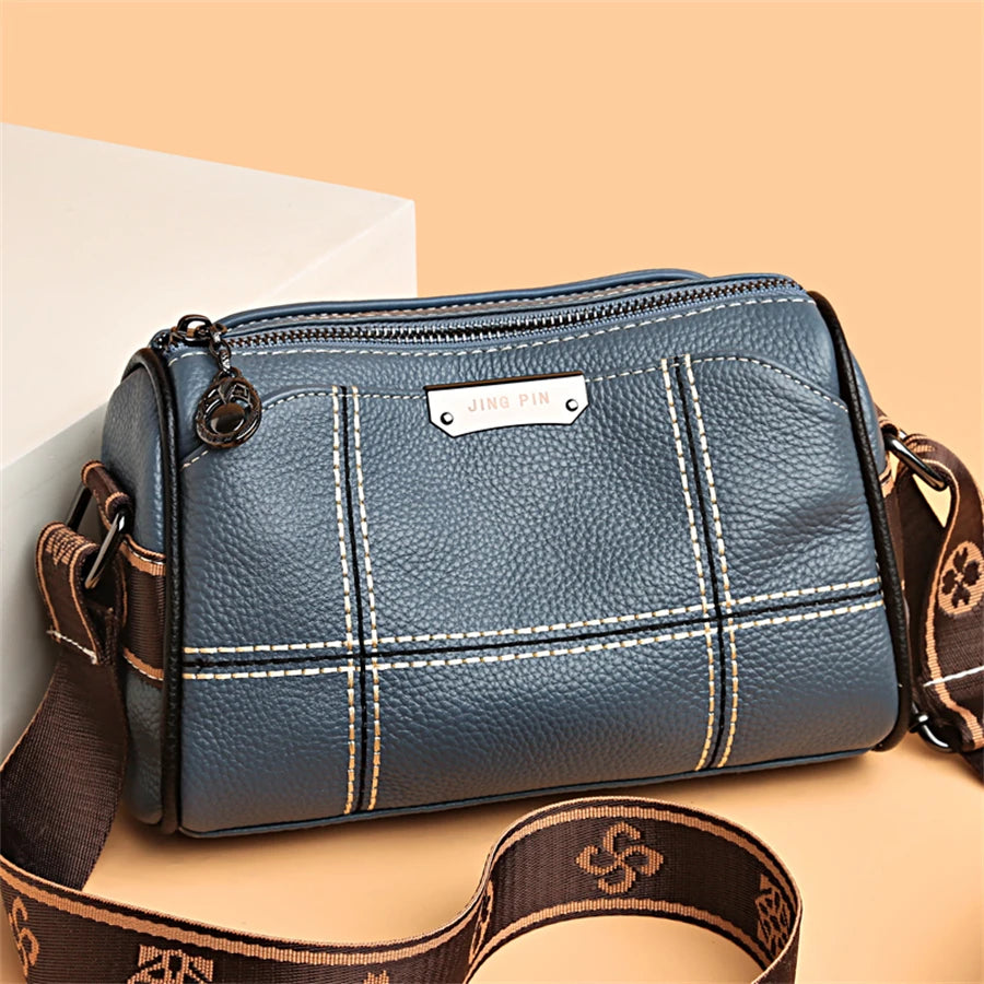 A dark blue leather shoulder bag with gold stitching and a brown strap resting on a light background.
