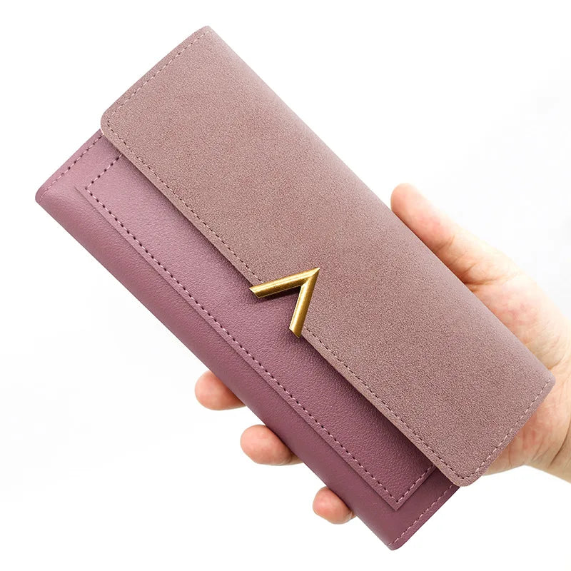 A mauve tri-fold PU card holder wallet with a gold signature design being held by a hand.