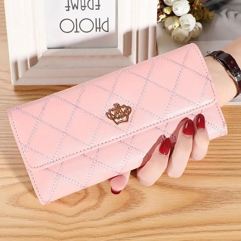 A pink quilted wallet with a gold crown buckle is shown resting on a wooden surface.