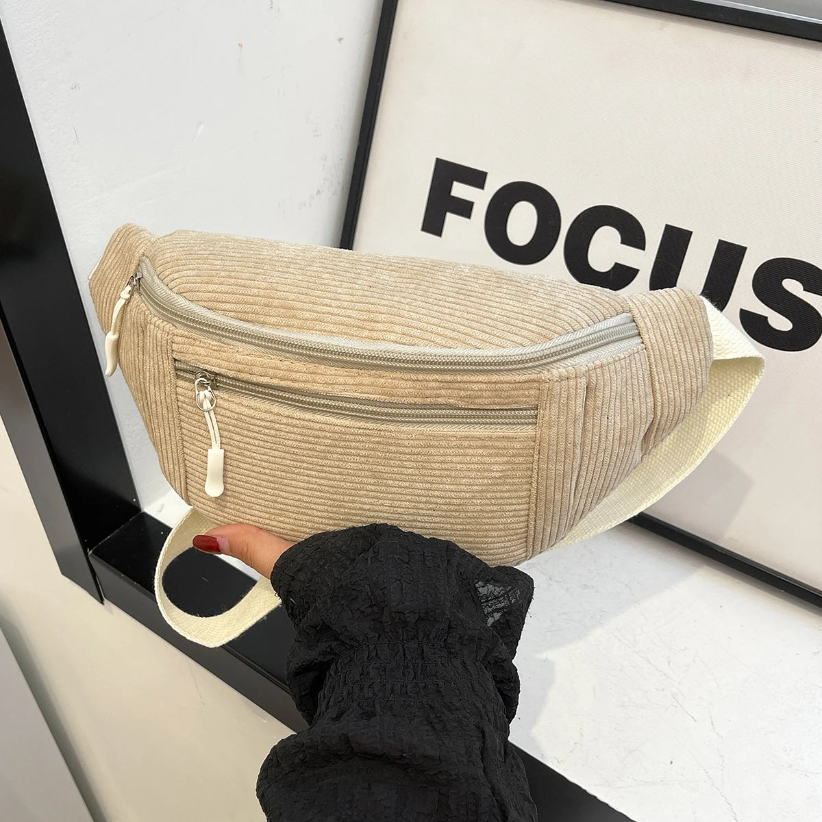 A beige corduroy crossbody waist bag with a zipper and adjustable strap is displayed against a white background.