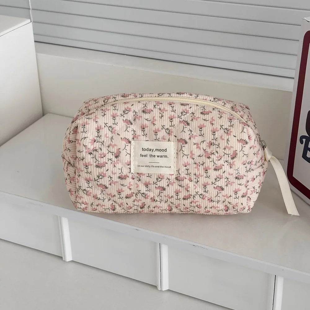 A pink floral print quilted cosmetic bag with a white tag resting on a white shelf.