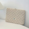 Funda acolchada floral beige para portátil sobre una superficie blanca.