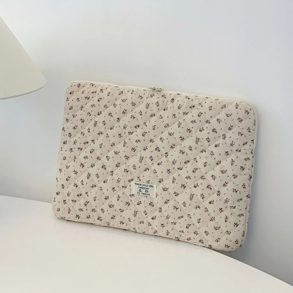 Funda acolchada floral beige para portátil sobre una superficie blanca.