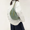 A woman wearing a light gray hoodie and dark pants carrying an olive green corduroy waist pack.