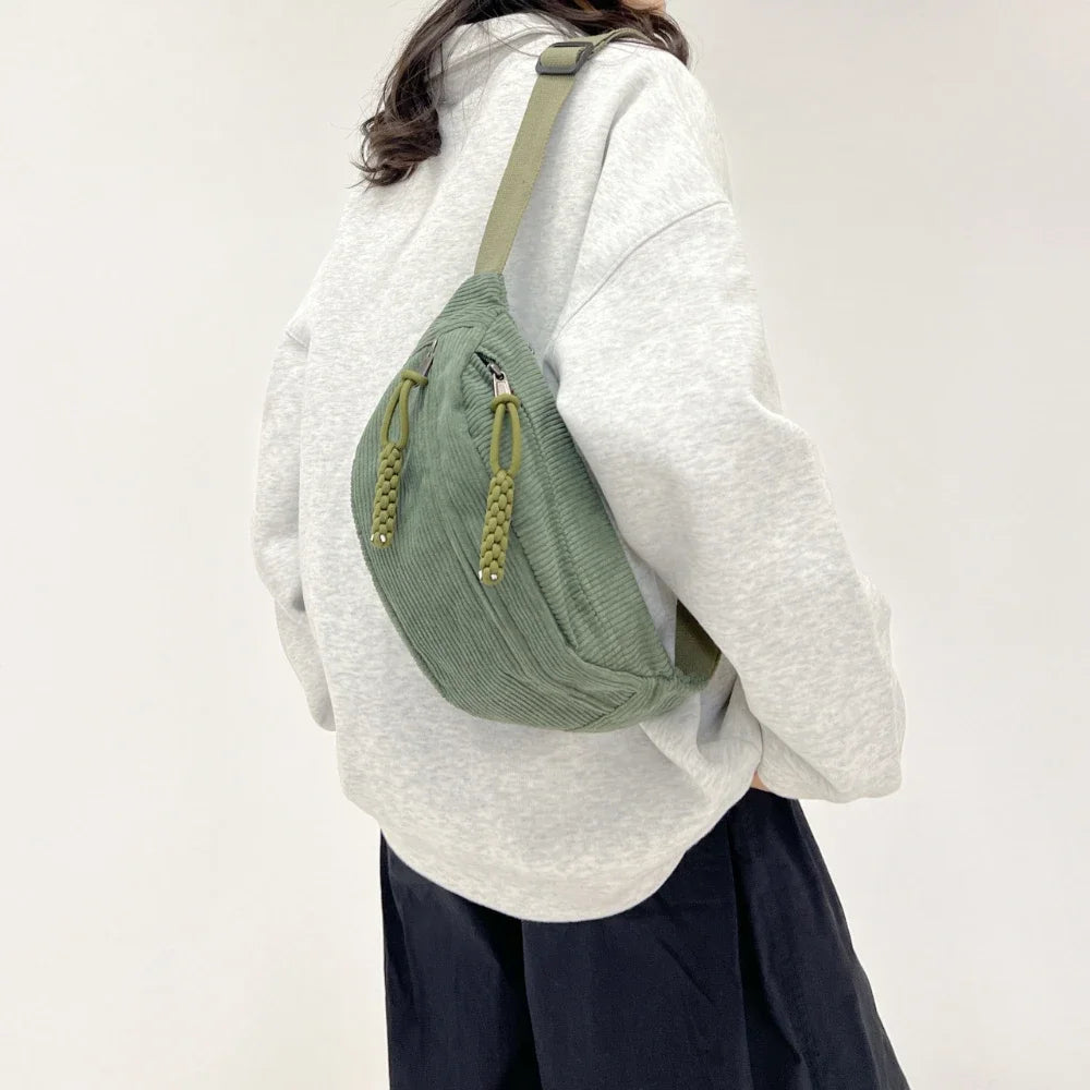 A woman wearing a light gray hoodie and dark pants carrying an olive green corduroy waist pack.